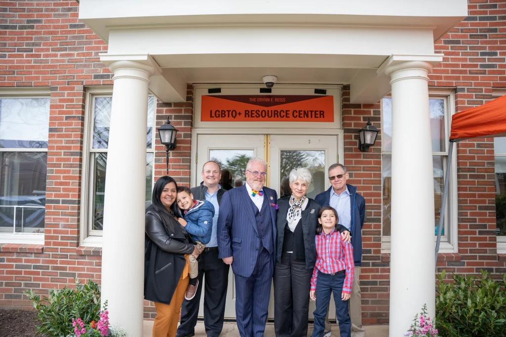 A group of seven people, including adults and children, stands in front of a building with a sign reading 