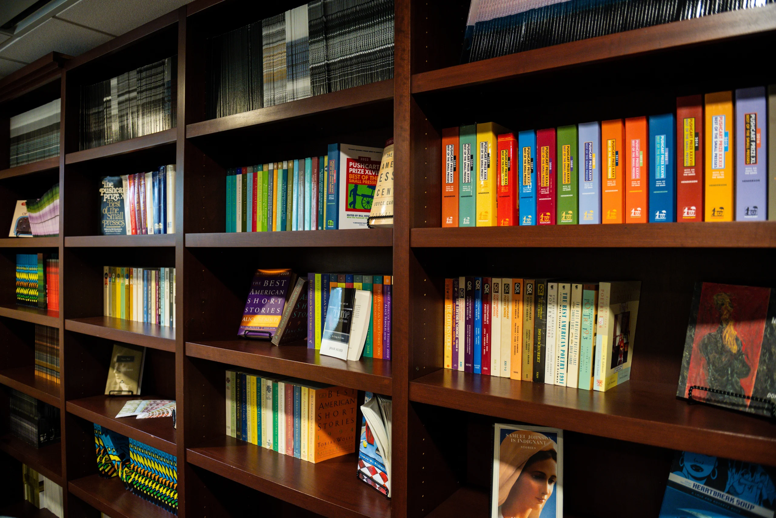 Wooden bookshelves filled with colorful books arranged by size and color, with a few decorative items placed among them.