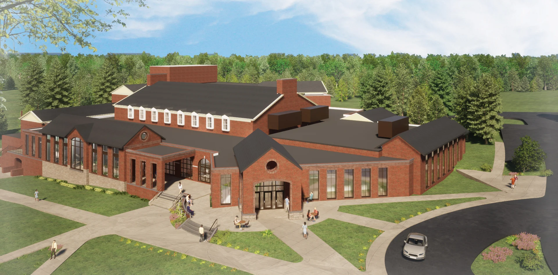 Aerial view of a large brick building with multiple entrances, surrounded by green lawns, trees, walkways, and people approaching the entrances.