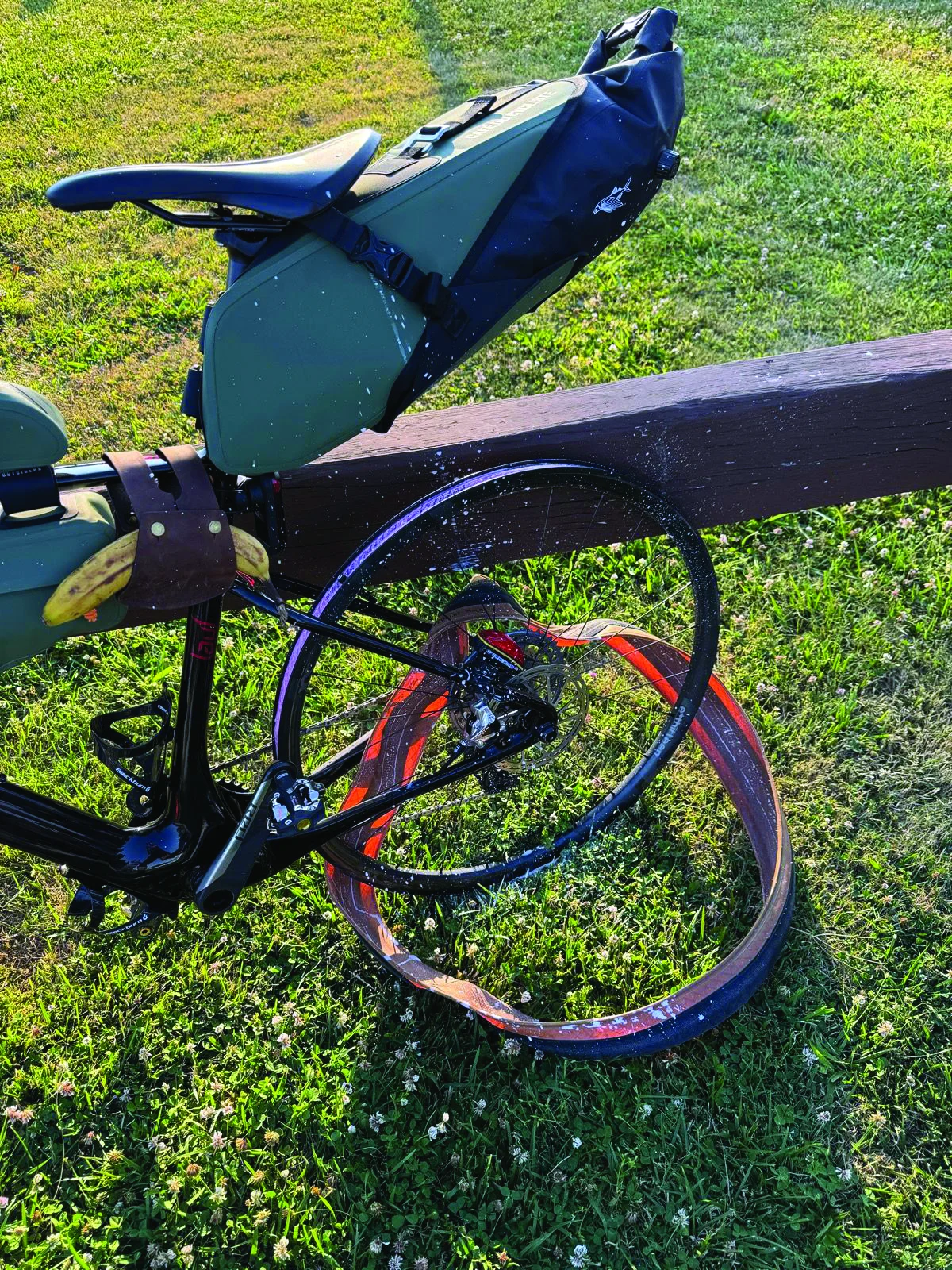 A bicycle with a severely bent and damaged rear wheel is resting against a wooden rail on green grass.