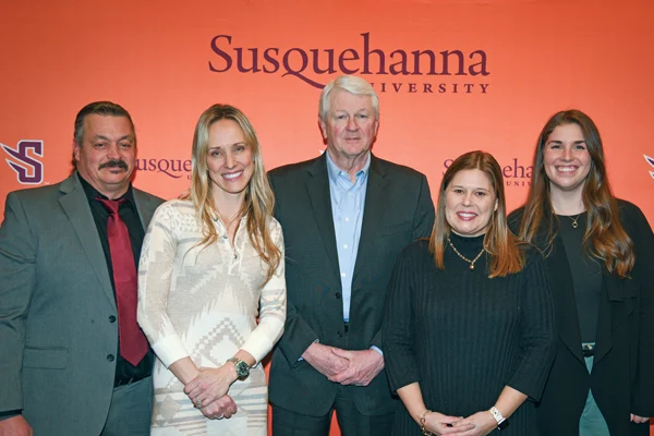 Five people stand in front of an orange backdrop displaying 