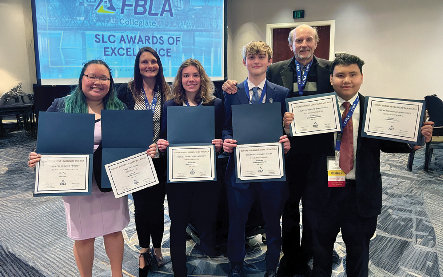 Six individuals standing in a line, each holding certificates, with a banner reading
