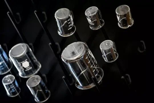 A collection of variously sized transparent beakers on a black background. The beakers are displayed upside down and have measurement markings on them.