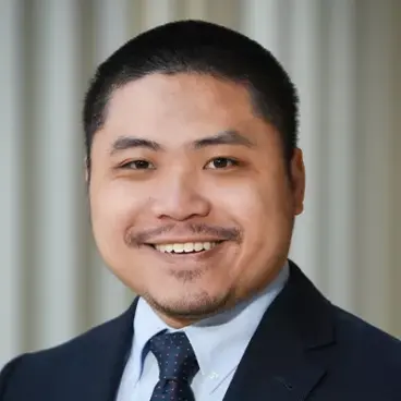 Smiling person in a suit and tie against a neutral background.
