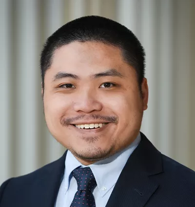 Smiling person in a suit and tie against a neutral background.