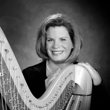 A black and white portrait of a person smiling, standing beside a harp. They have shoulder-length hair and are wearing a dark top. Their hands are gently resting on the harp. The background is softly textured.