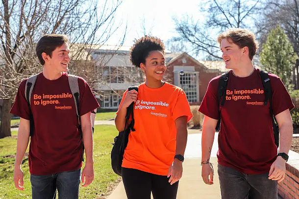 Three students walk outdoors wearing t-shirts with the slogan 