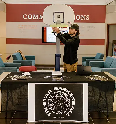 A person adjusts a mini basketball hoop on a table with a 