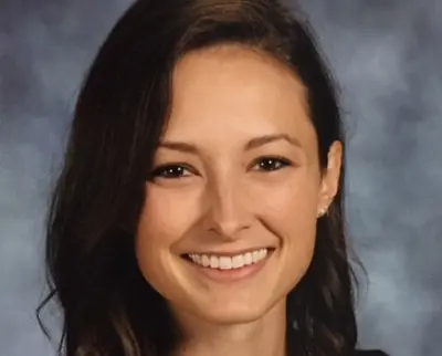 A person with long brown hair is smiling against a gray and blue background.