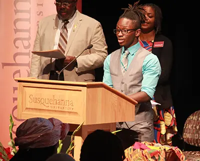 A young individual speaks at a podium labeled 