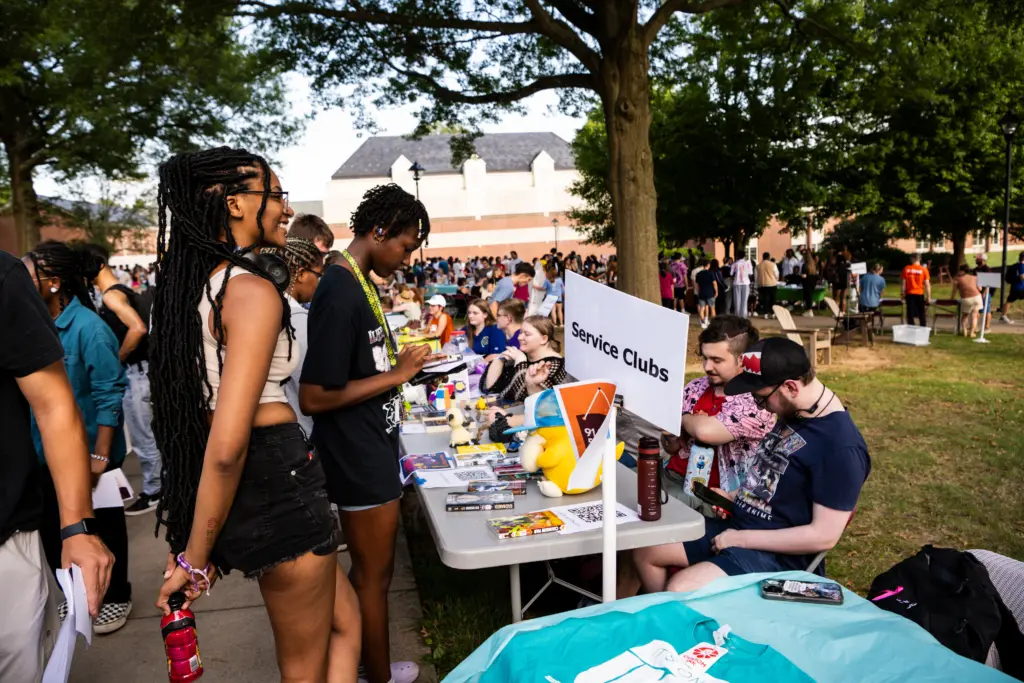 People are gathered outdoors at a community or school event. A table labeled 