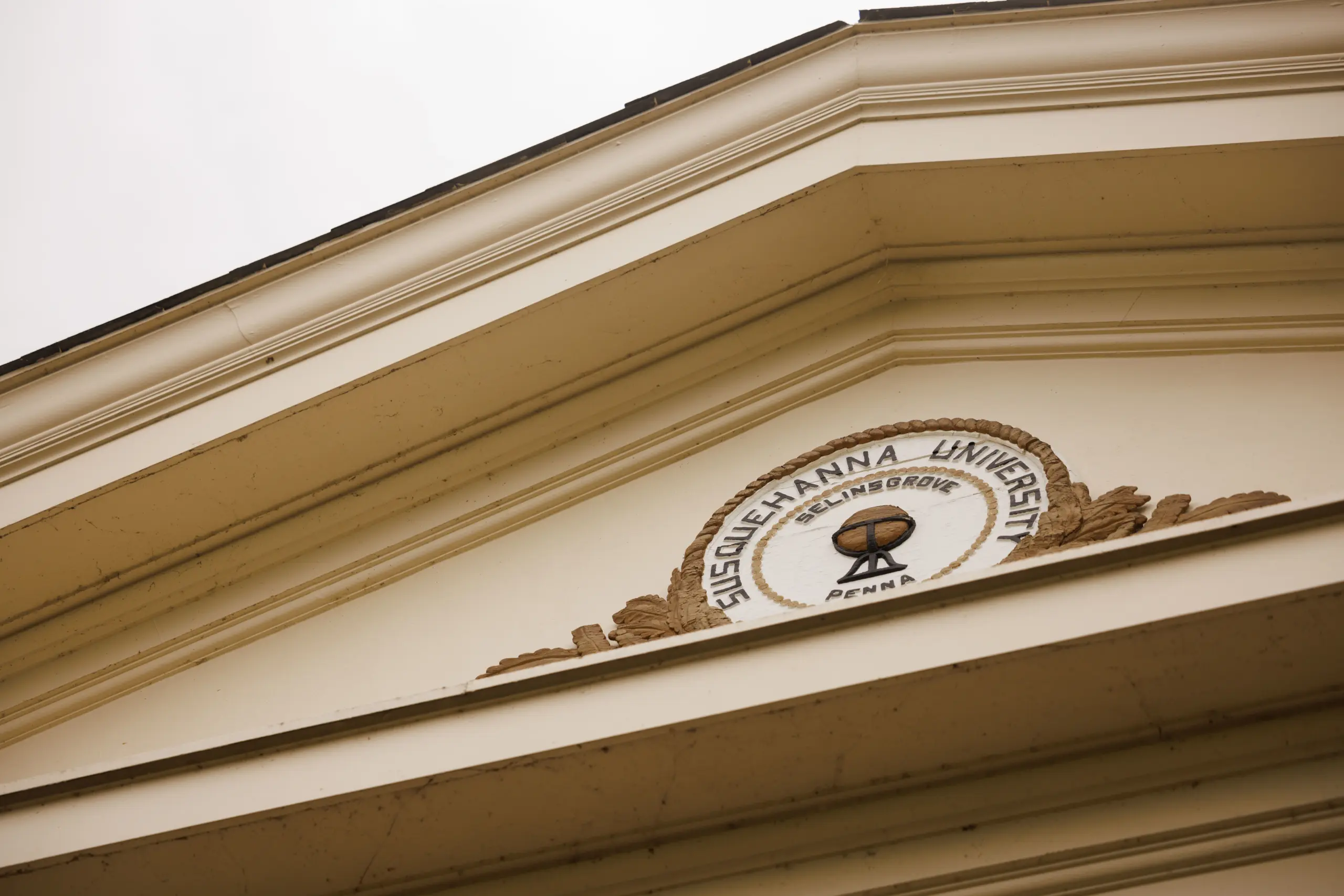 A triangular architectural pediment with the seal of 体育买球 University. The seal features a globe and text reading