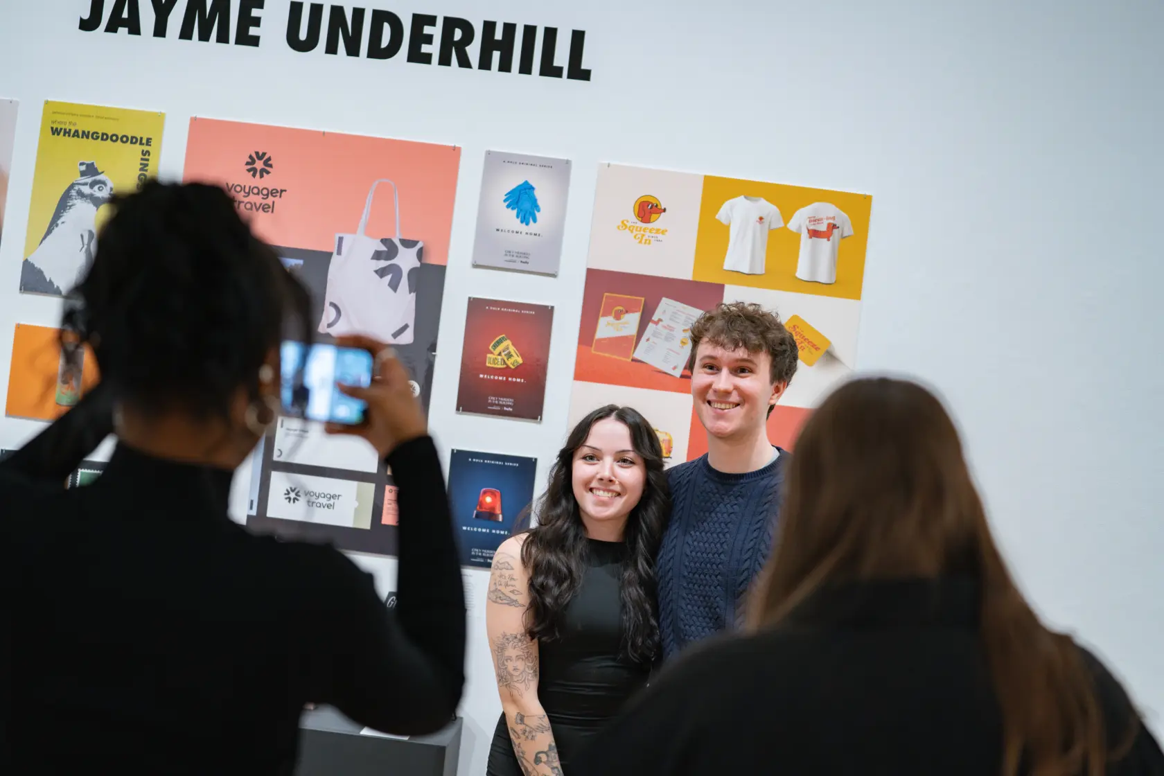 Arts Administration students pose for a photo, smiling, in front of a display featuring various graphic designs