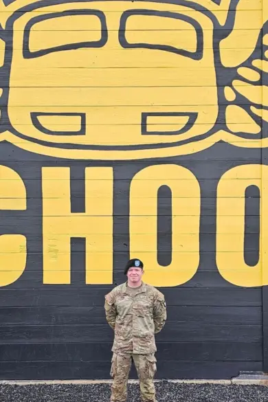 A person in military uniform stands in front of a large wall mural depicting a stylized yellow car with wings, with the word 