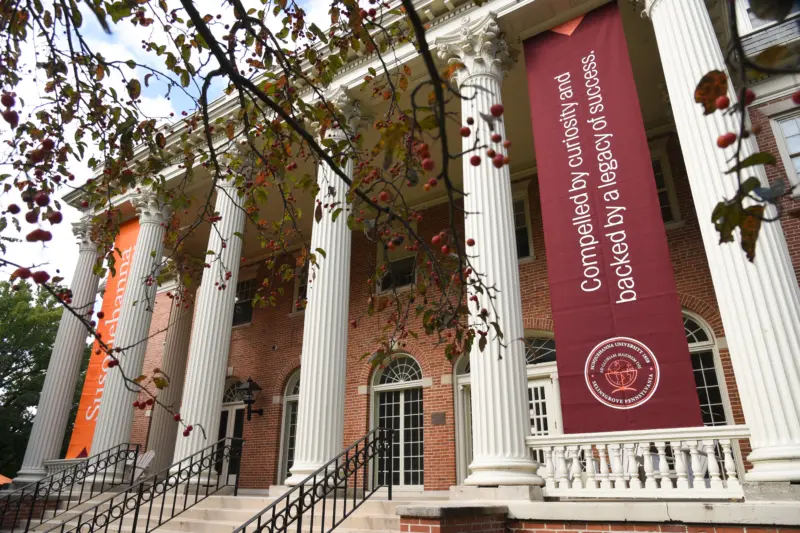 A grand building with tall white columns and red brick facade captivates viewers. One large banner reads, 
