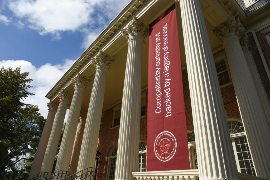 A historic building with large columns and a red banner hanging between them. The banner reads, 