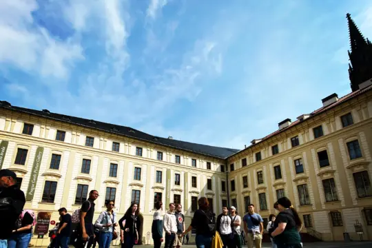 A group of tourists immersed in conversation fills a spacious courtyard surrounded by historic buildings with ornate facades under a bright blue sky, as if preparing for their next GO Study Abroad adventure.