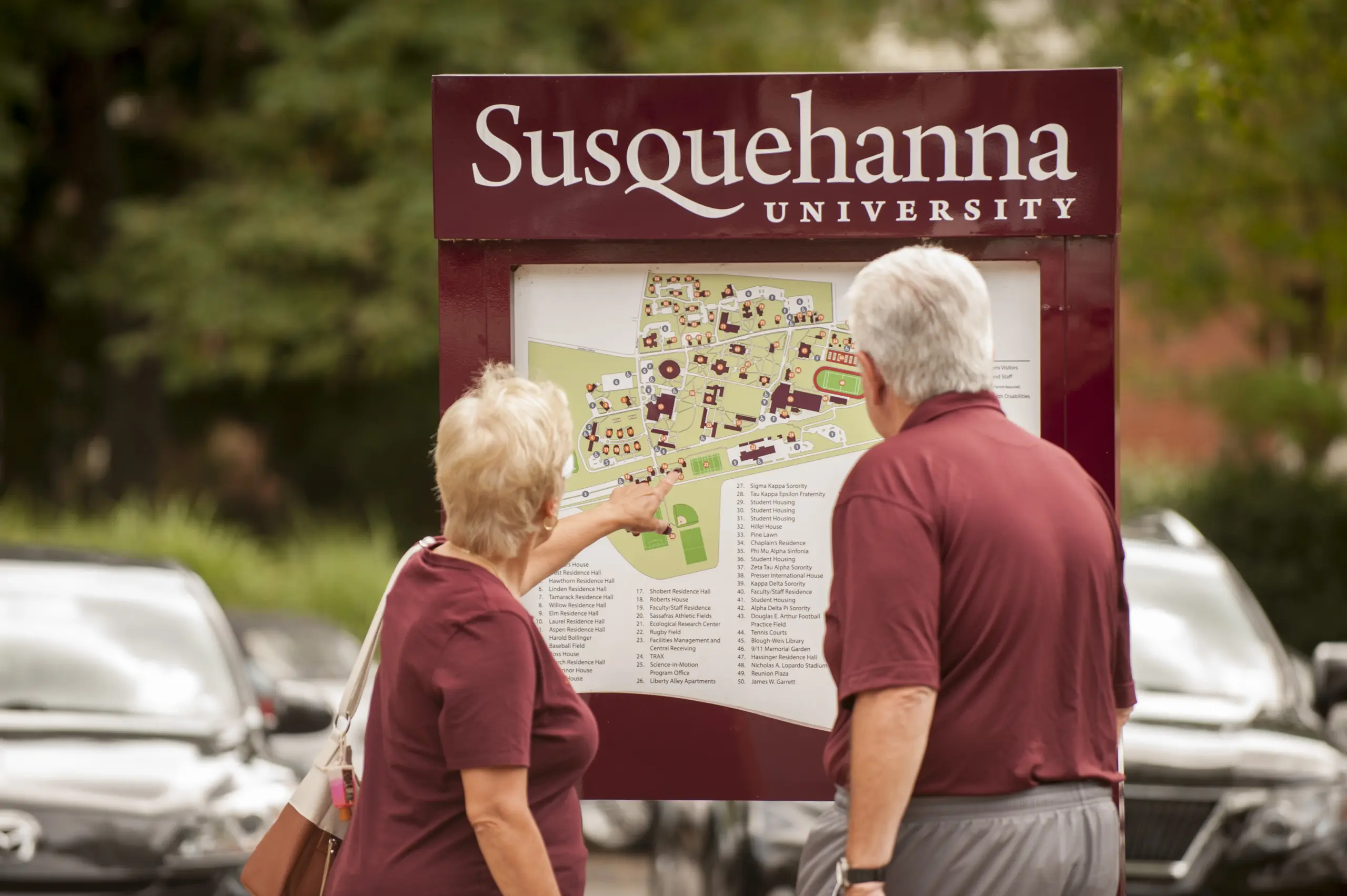 Two people in maroon shirts consult the Maps and Directions sign labeled 