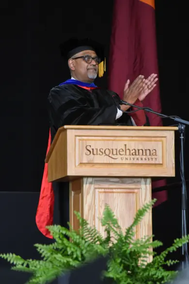 A person in academic regalia stands at a podium with 