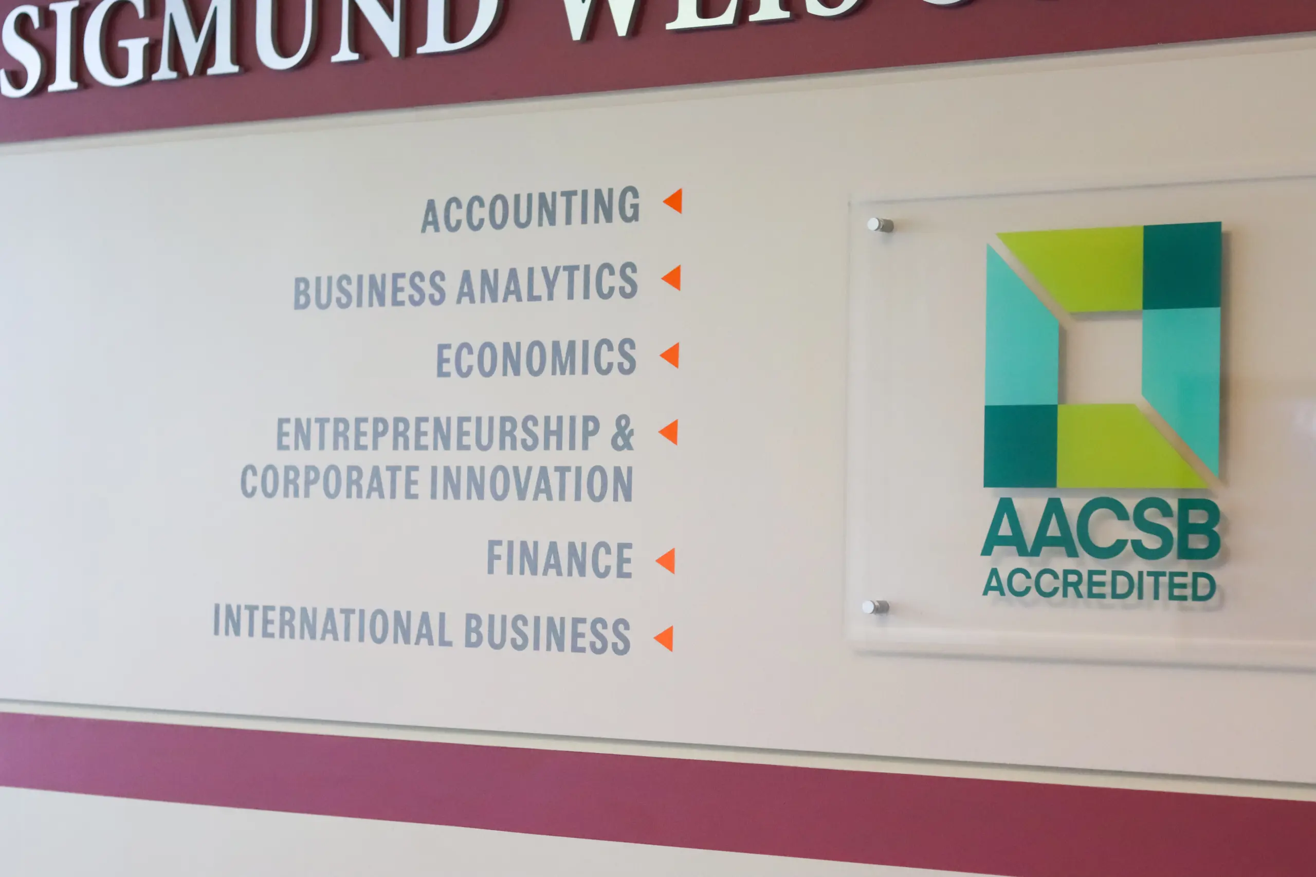 Wall sign highlighting academic programs—Accounting, Business Analytics, Economics, Entrepreneurship & Corporate Innovation, Finance, and International Business—stands beside an AACSB Accredited plaque, underscoring a strong commitment to academics.