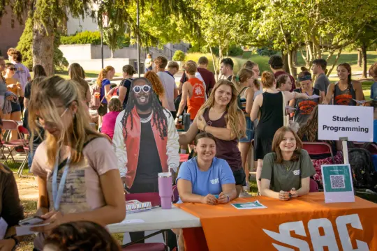 Outdoor college fair buzzing with students at activity booths. Embracing campus life, three smiling people at a 