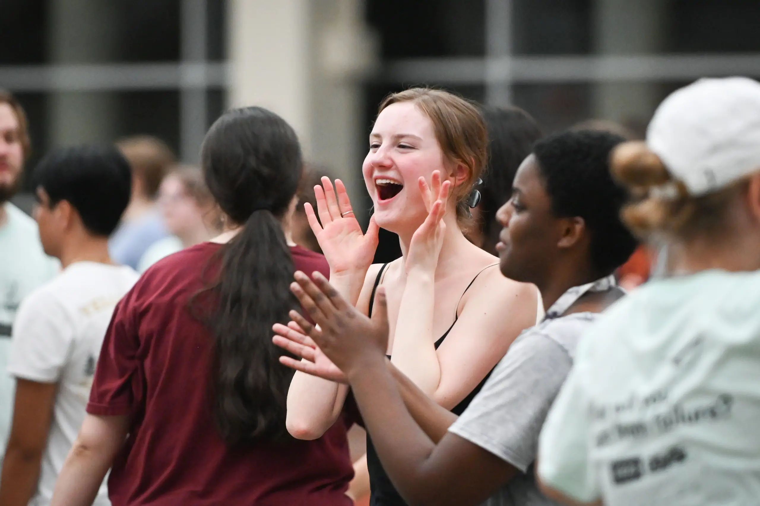 A young woman in a black top cheers and claps enthusiastically among a group of people, some also clapping, during the lively 体育买球官网 Success Day indoor event.
