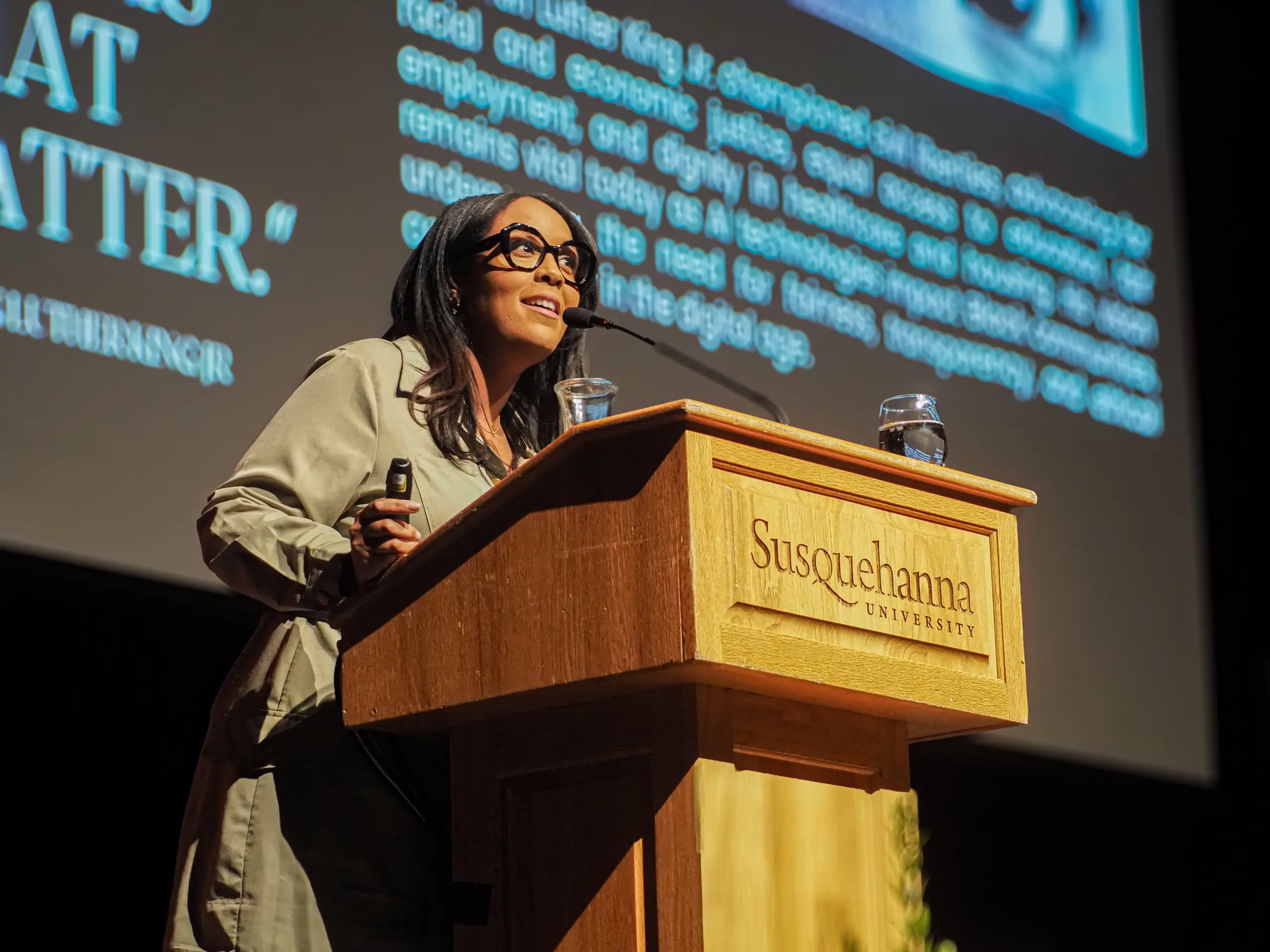A woman speaks at a wooden podium inscribed with 