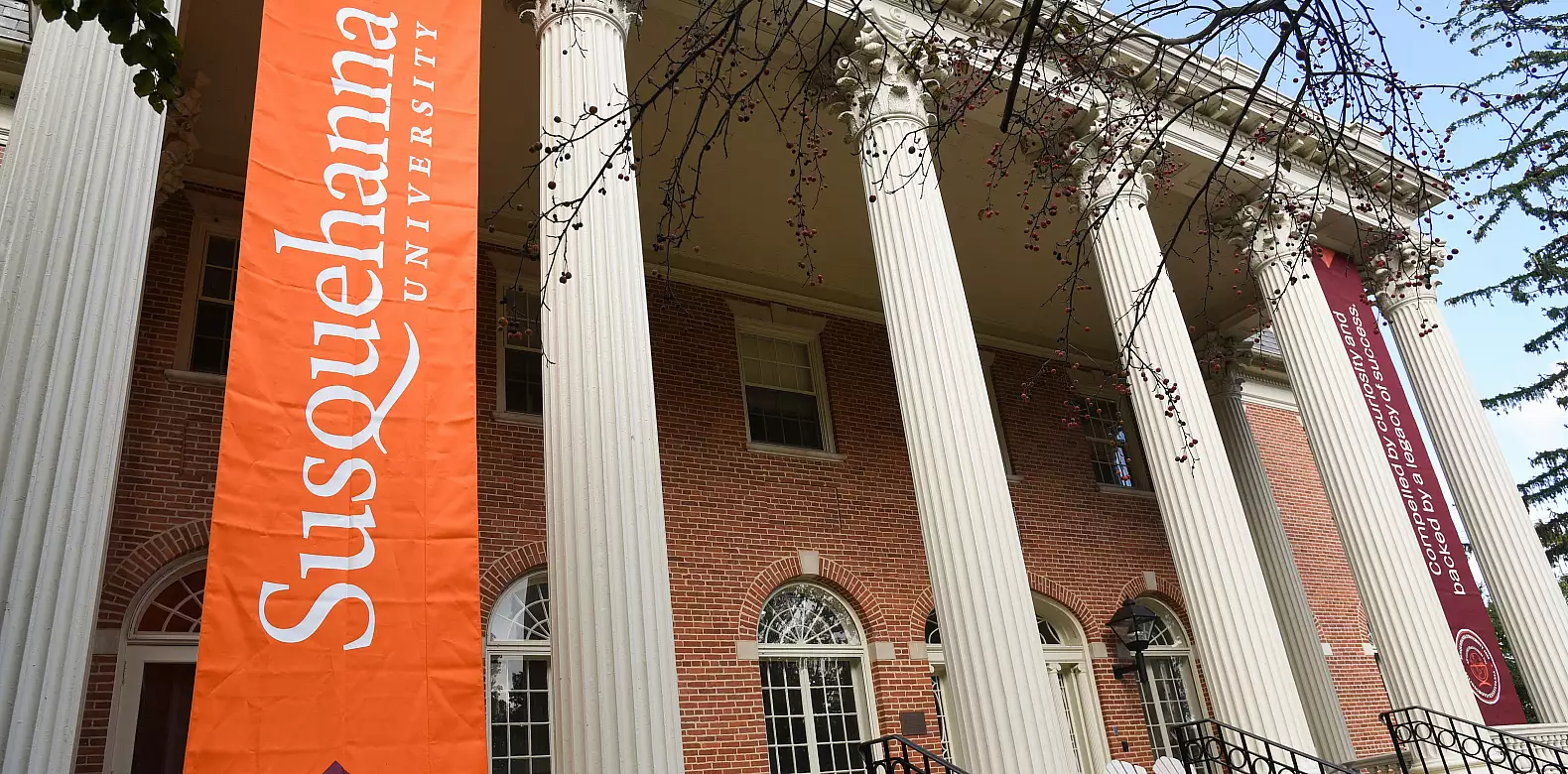 A brick building with tall white columns displays large banners reading 