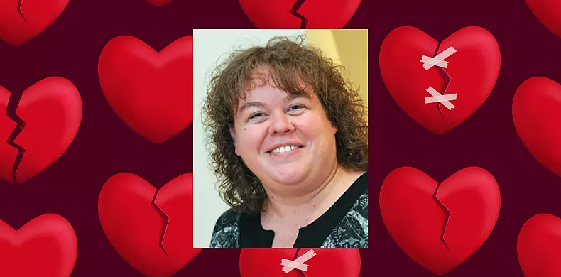 A woman with curly hair smiles at the camera. The background features a pattern of large, red, broken hearts on a dark backdrop, with one heart taped together.