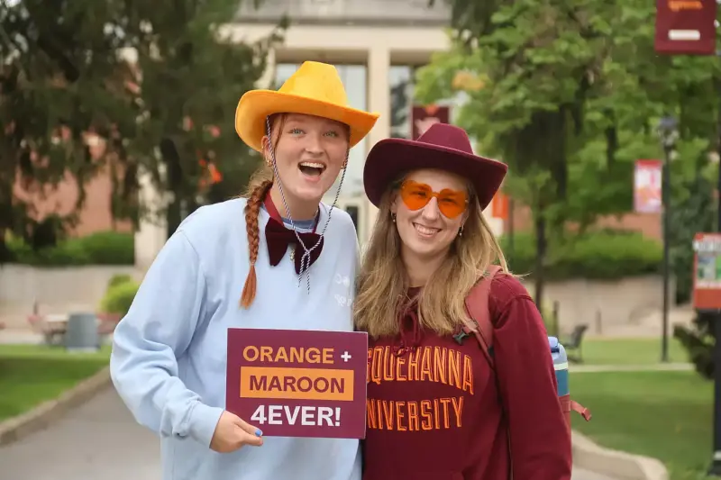 Two smiling people in cowboy hats and sunglasses pose outdoors, one holding a 