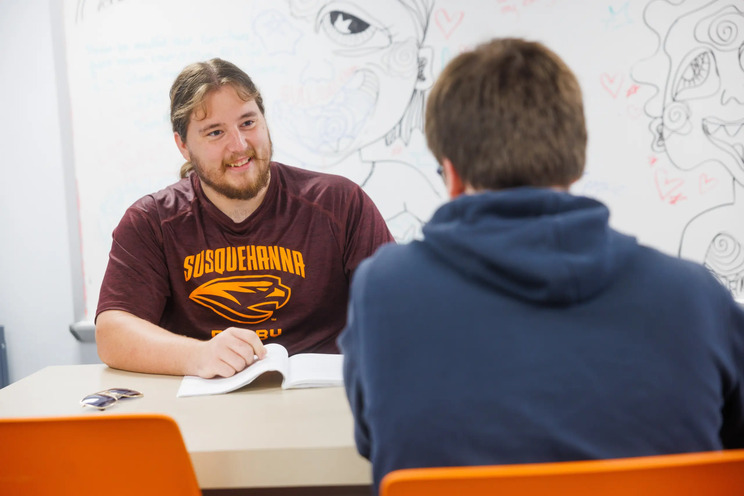 Two people sit across from each other at a table, one wearing a