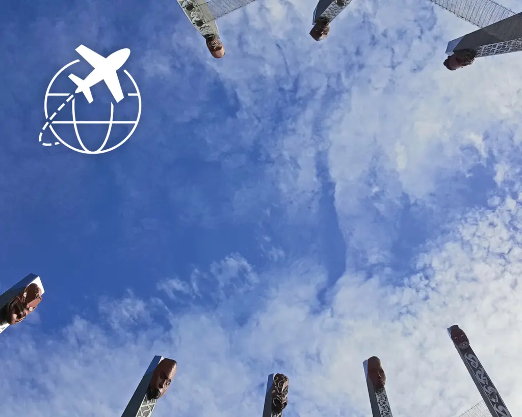 Photo of tall carved pillars with faces, arranged in a circle and viewed from below against a blue sky with clouds; an 