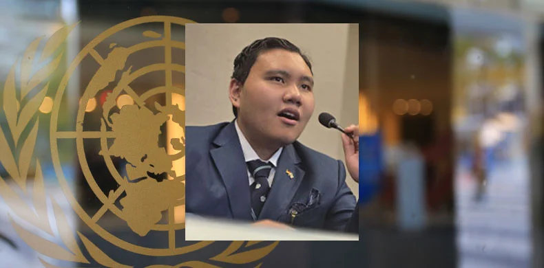 A young man in a suit speaks into a microphone. His photo is overlaid on a window featuring the United Nations emblem, with a blurred background visible through the glass.
