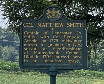 Historic marker sign for Col. Matthew Smith, noting he was a captain with Benedict Arnold in 1775, later vice-president of Pennsylvania Council, died in 1794, and is buried in an unmarked grave. Trees and fields are visible in the background.