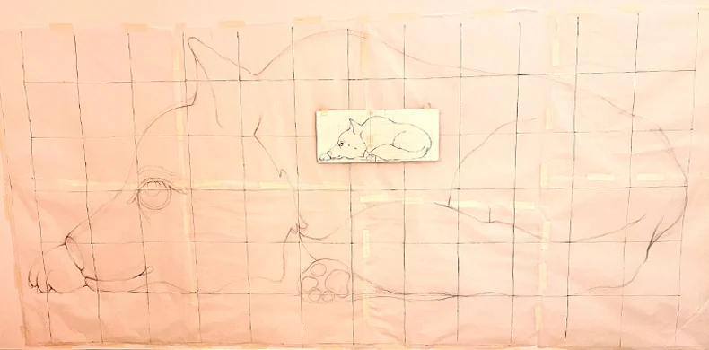 A large, grid-lined paper shows the outline of a lying dog. At the center, a small paper with a similar dog sketch is taped on, also gridded, serving as a reference for the larger drawing.