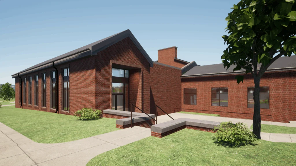 A modern red-brick building with large windows and sloped roofs sits on a green lawn, showcasing recent campus transformations, with sidewalks and a few shrubs under a clear blue sky.