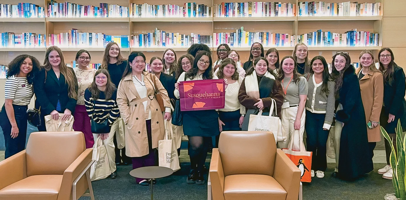 A group of women pose together in front of bookshelves, some holding tote bags and a red 体育买球官网 sign, in a library or bookstore setting.